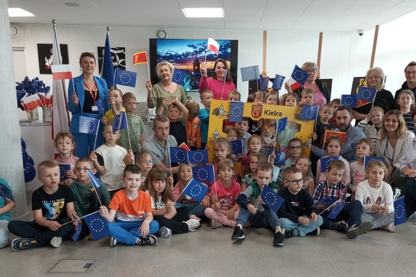 zdjęcie przedstawia grupę dzieci w punkcie promocji Kielc z flagami Unii Europejskiej