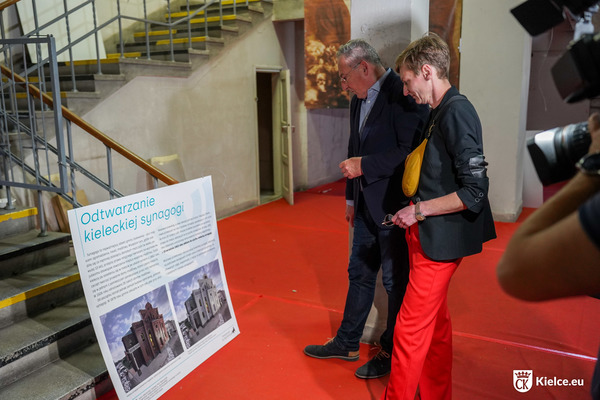 zdjęcie; prezydentka Agata Wojda i były minister kultury Bartłomiej Sienkiewicz oglądają tablicę historyczną przedstawiającą zdjęcia budynku dawnej synagogi