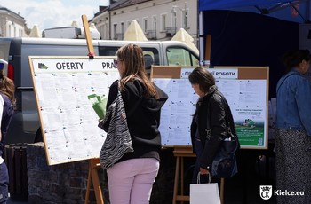 Zdjęcie przedstawia osoby poszukujące pracy, czytające oferty pracy z tablicy informacyjnej na Rynku