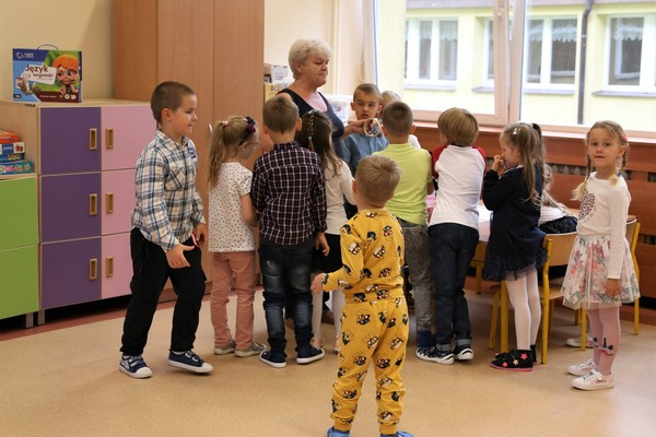 grupa dzieci w kolorowych strojach zgromadzona wokół nauczyciela