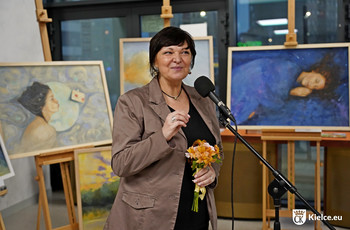 Autorka prac Agnieszka Łuczyńska stojąca przy mikrofonie, za nią ustawione są obrazy