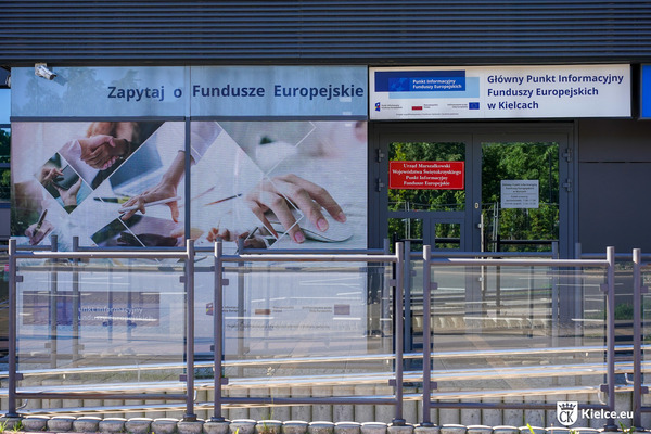 Fragment budynku, w którym mieści się Główny Punkt Informacyjny Funduszy Europejskich w Kielcach. Nad wejściem szyld z nazwą punktu, obok baner z napisem "Zapytaj o Fundusze Europejskie".